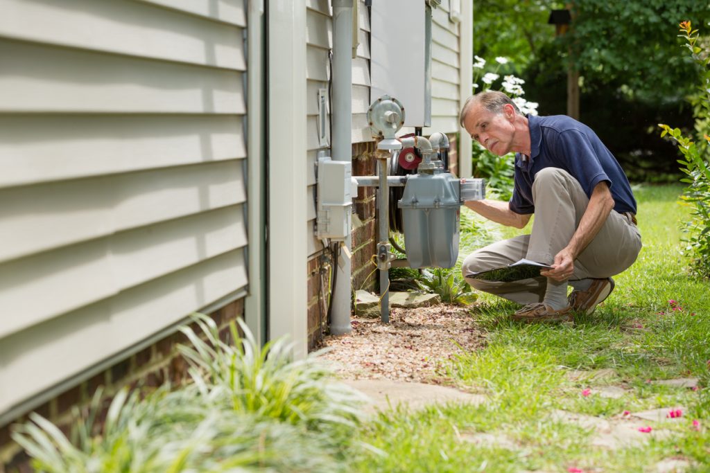 Home inspector, outside, examines a residential natural gas meter.